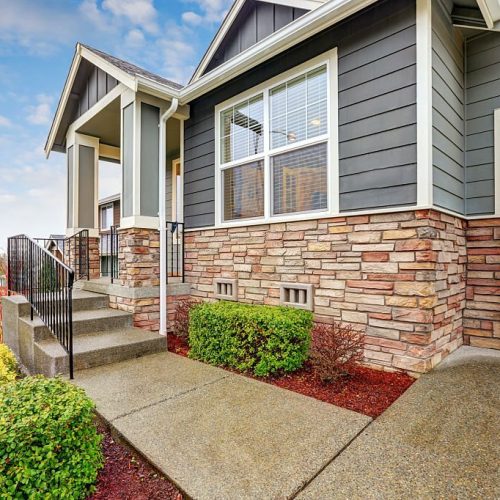 Gray house exterior with column porch and stone wall trim on a rainy day. Northwest, USA