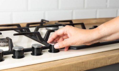 Close-up of a home cooking stove. Gas stove. Woman's hand turns on the kitchen gas stove.Industrial resources and economy concept.Side view. Space for text.Modern kitchen stove.